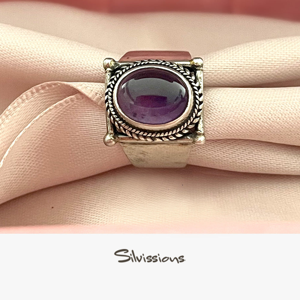 Silver ring with a purple gemstone on pink fabric, branded 'Silvissions'.