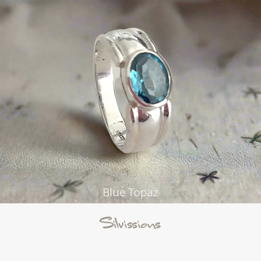 Silver ring with blue topaz gemstone on a textured fabric background, featuring the brand 'Silvissions'.