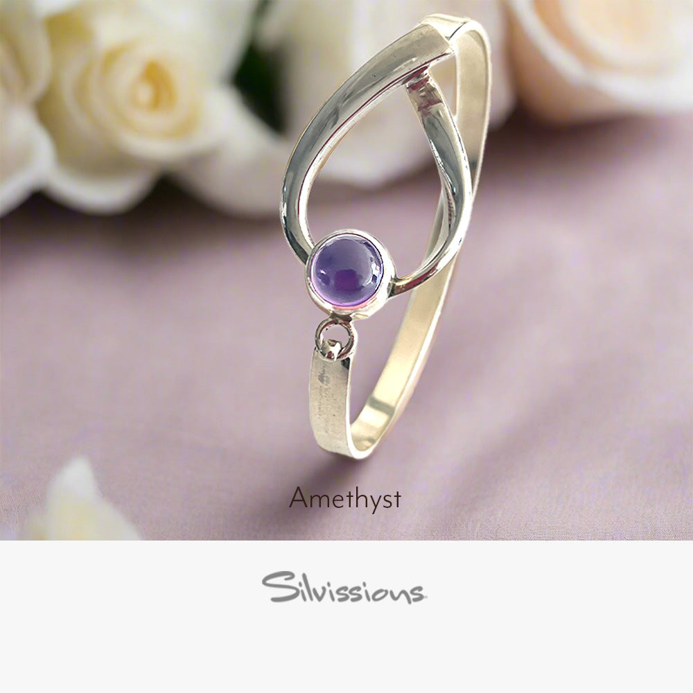 Silver ring with a purple gemstone on a soft pink background with white roses.