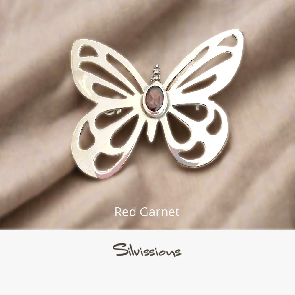 Silver butterfly brooch with red gemstone on a beige fabric background, branded 'Silvissions'.