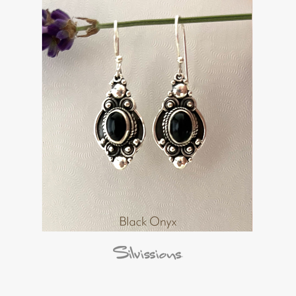 Silver earrings with black stones on a textured beige background, featuring the brand 'Silvissions'.