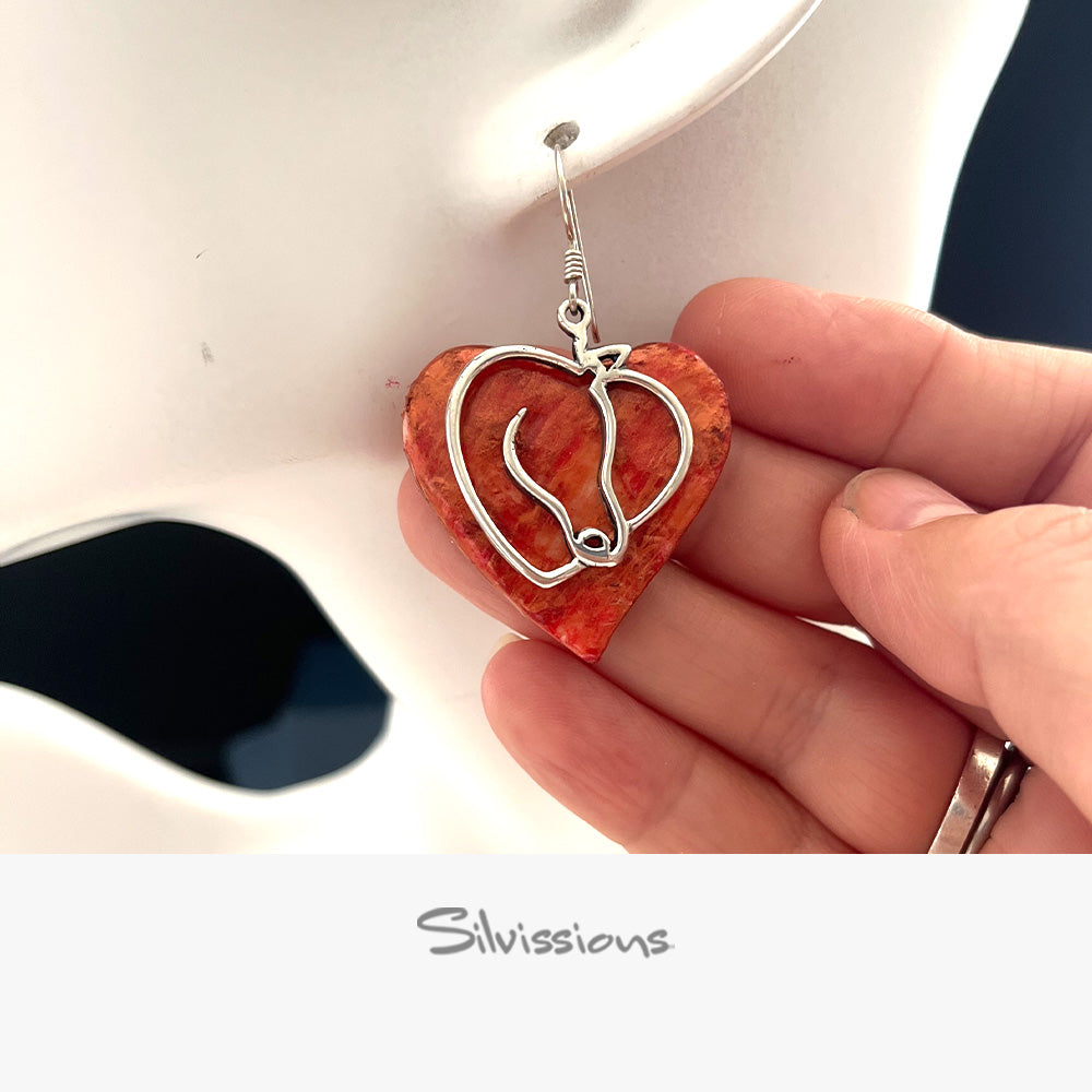 Heart-shaped earring with a silver horse design held by a hand, brand 'Silvissions' visible.