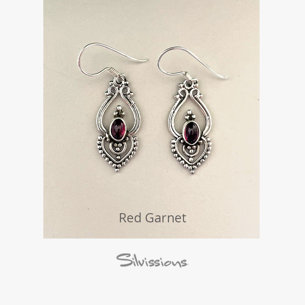A pair of sterling silver dangle earrings with red garnet oval gemstones, displayed against a backdrop.