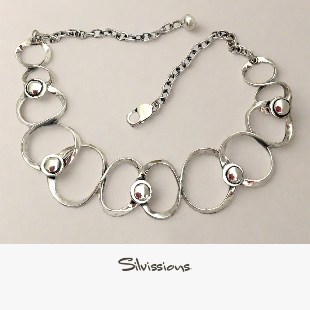 Silver necklace with circular links and embedded beads on a beige background, branded 'Silvissions'.
