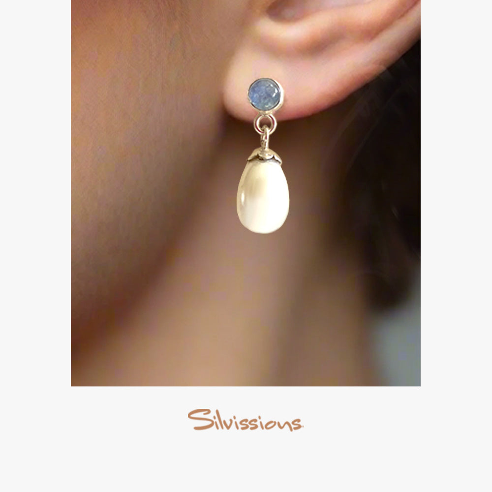 Close-up of an ear wearing a pearl and blue stone earring.
