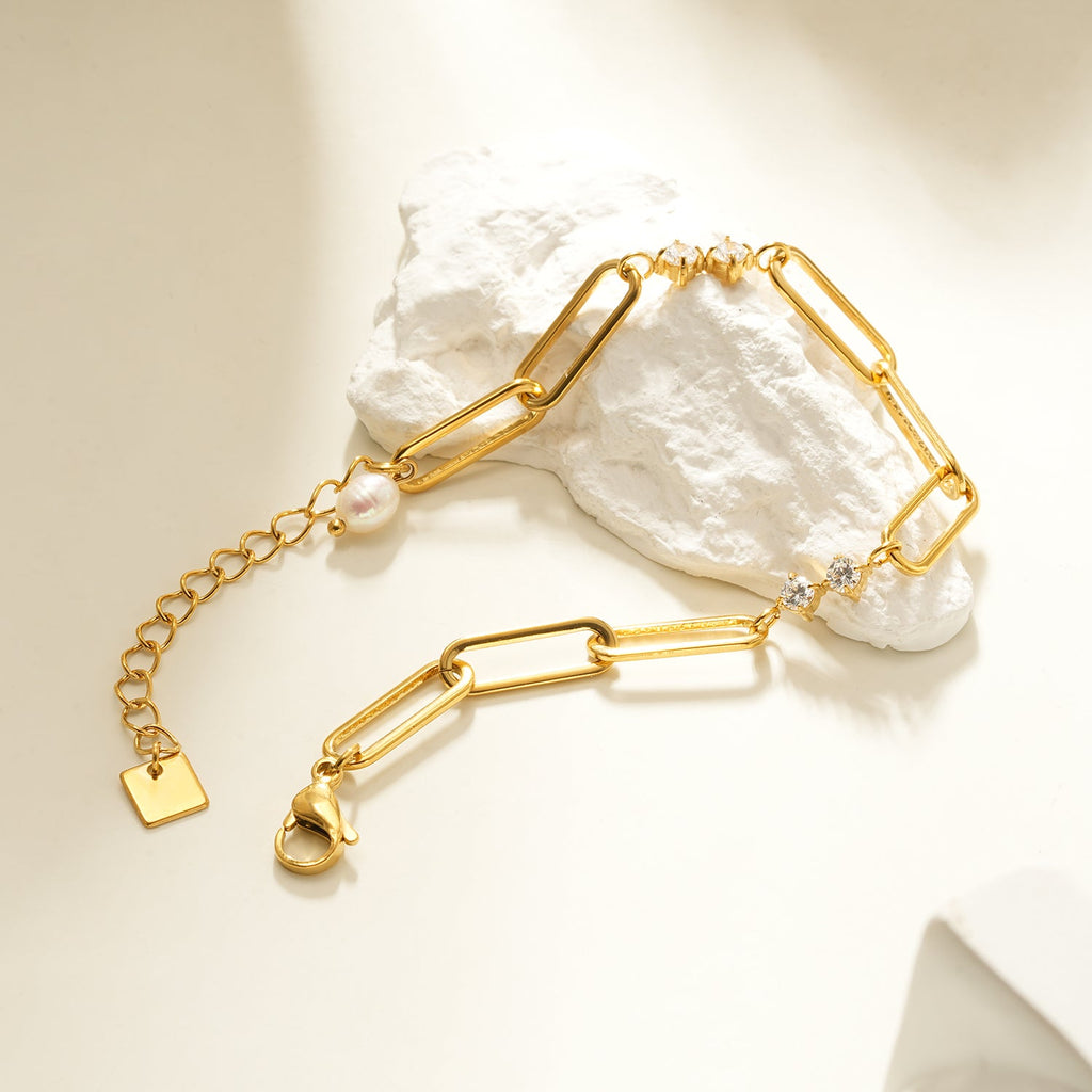 Gold bracelet with pearl and gemstone accents on a textured white surface