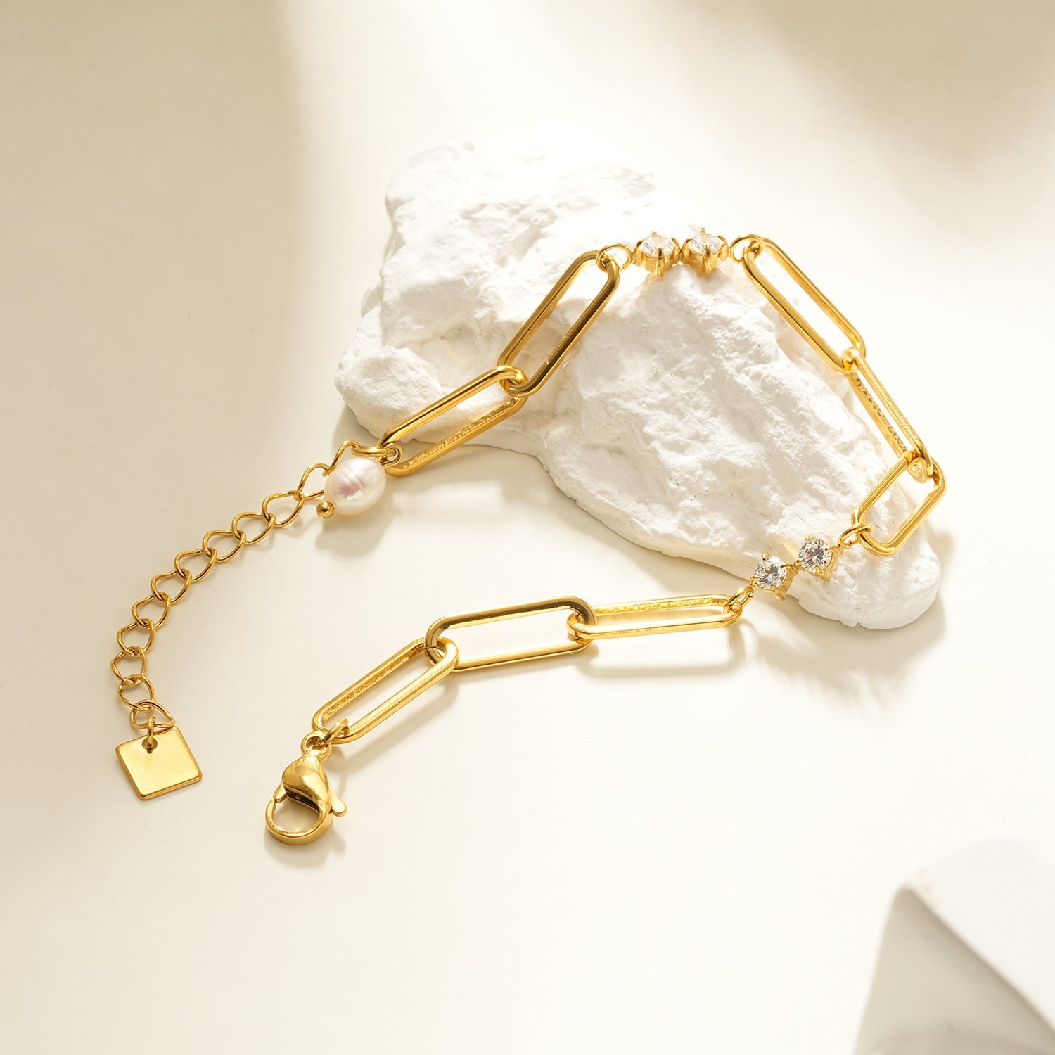 Gold bracelet with pearl and gemstone accents on a textured white surface