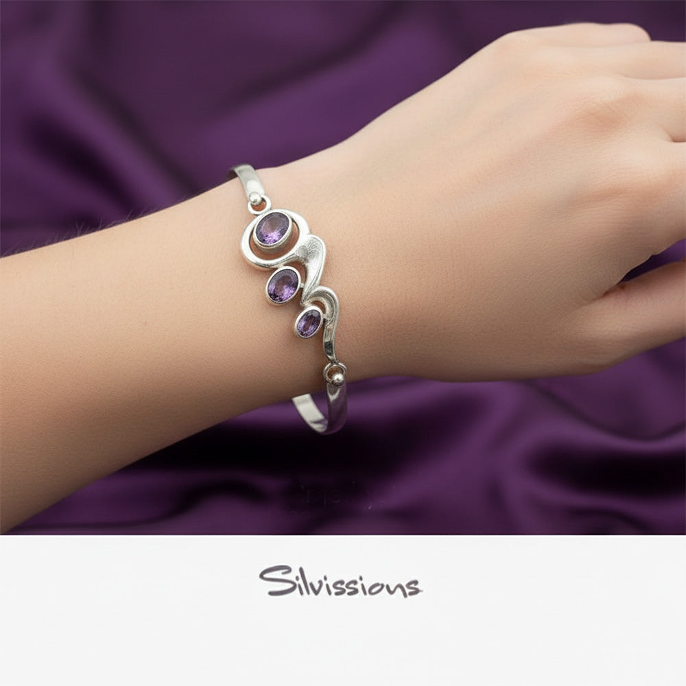 Silver bracelet with purple stones on a wrist against a purple fabric background, featuring the brand 'Silvissions'.