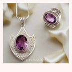 Silver-tone filigree jewelry set featuring an oval pendant necklace and matching ring, both with a purple amethyst stone, displayed on a soft cream satin background. The brand name 'SILVISSIONS' is visible at the bottom.