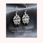 Silver lotus flower earrings with black onyx stones on a gray surface, branded 'Silvissions'.