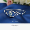 Silver bracelet with blue topaz gemstone on a blue fabric background, featuring the brand 'Silvissions'.