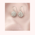 Silver bridal earrings on a pink fabric background with 'Silvissions' branding.