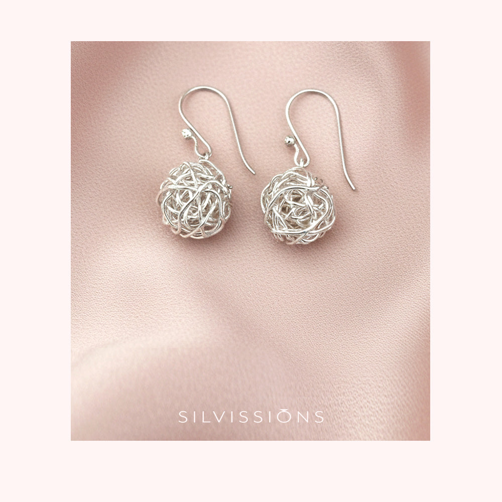 Silver bridal earrings on a pink fabric background with 'Silvissions' branding.