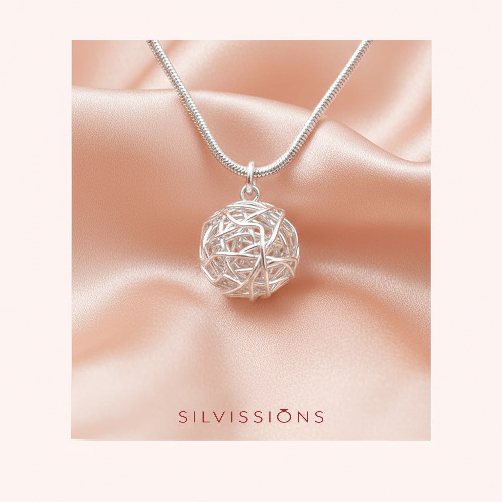 Silver necklace with a intricate pendant on a soft pink background, featuring the brand 'Silvissions'.