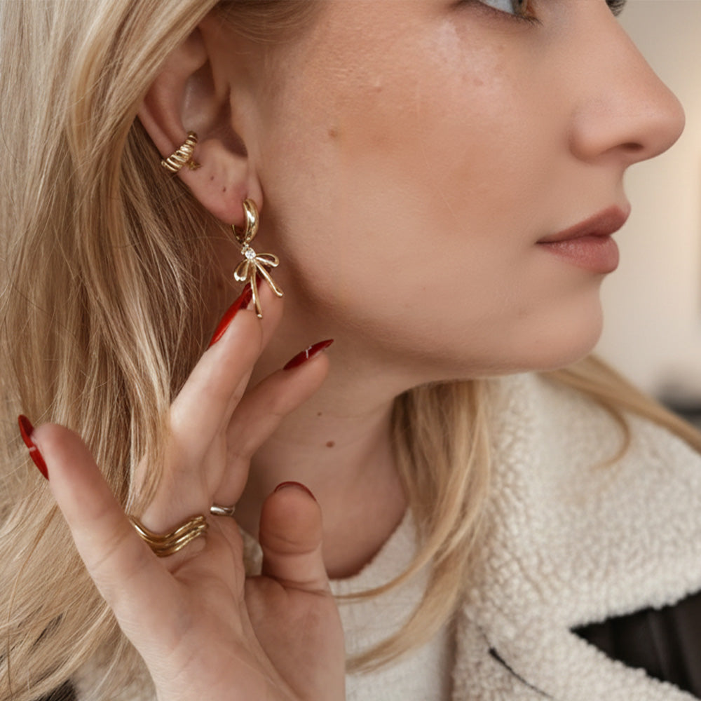 Close-up of a woman wearing gold earrings and rings, with a blurred background.