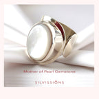 Silver ring with mother of pearl gemstone on white fabric, featuring Silvissions brand.