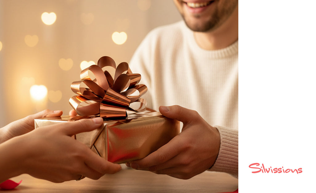 Person receiving a gift wrapped in gold paper with a large bow, blurred lights in the background