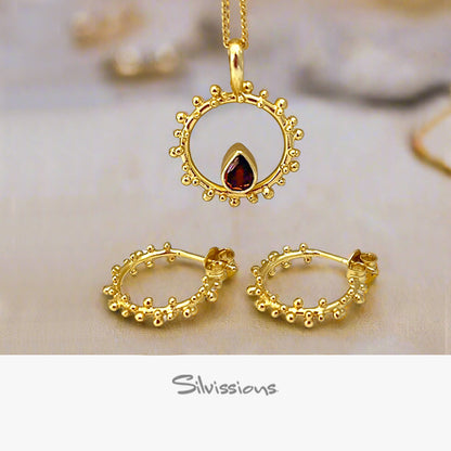 Gold jewelry set with pendant, hoop earrings, and necklace on a soft background.