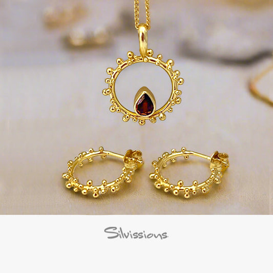 Gold jewelry set with pendant, hoop earrings, and necklace on a soft background.