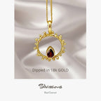 A gold-plated sterling silver pendant necklace with a red garnet gemstone in a circular design, displayed on a person wearing a red garment.