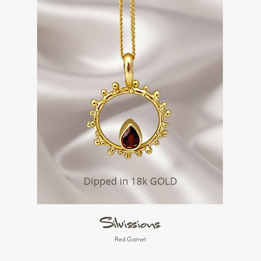 A gold-plated sterling silver pendant necklace with a red garnet gemstone in a circular design, displayed on a person wearing a red garment.