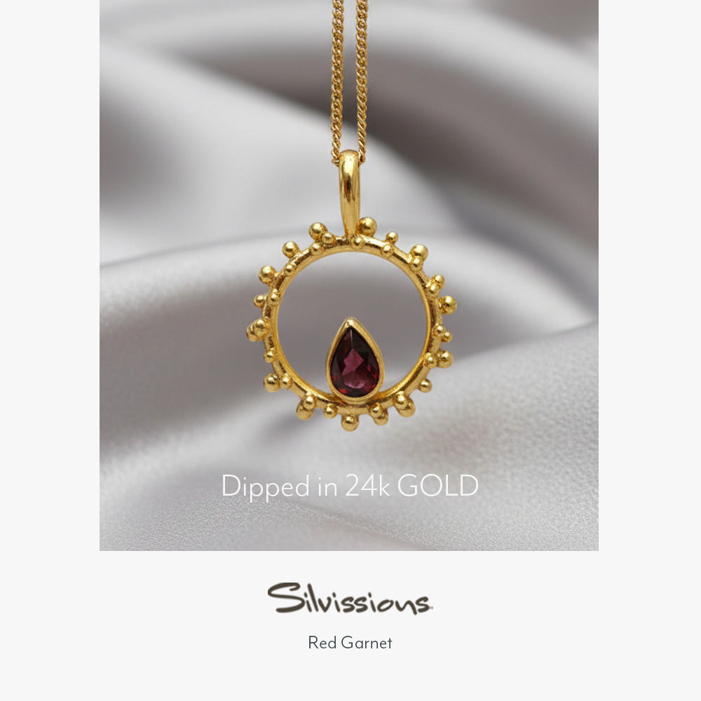 A gold-plated sterling silver pendant necklace with a red garnet gemstone in a circular design, displayed on a person wearing a red garment.