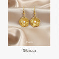 Gold earrings with pearls on a satin background, featuring the brand 'Silvissions'.