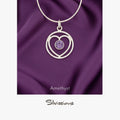 A sterling silver heart-shaped pendant necklace with an amethyst gemstone in the center, displayed against a purple background with the brand name 'Silvissions' mentioned at the bottom.