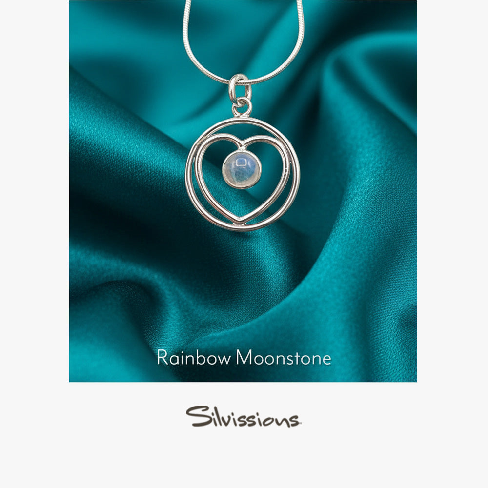 Silver pendant with heart design and rainbow moonstone on teal fabric, featuring the brand 'Silvissions'.