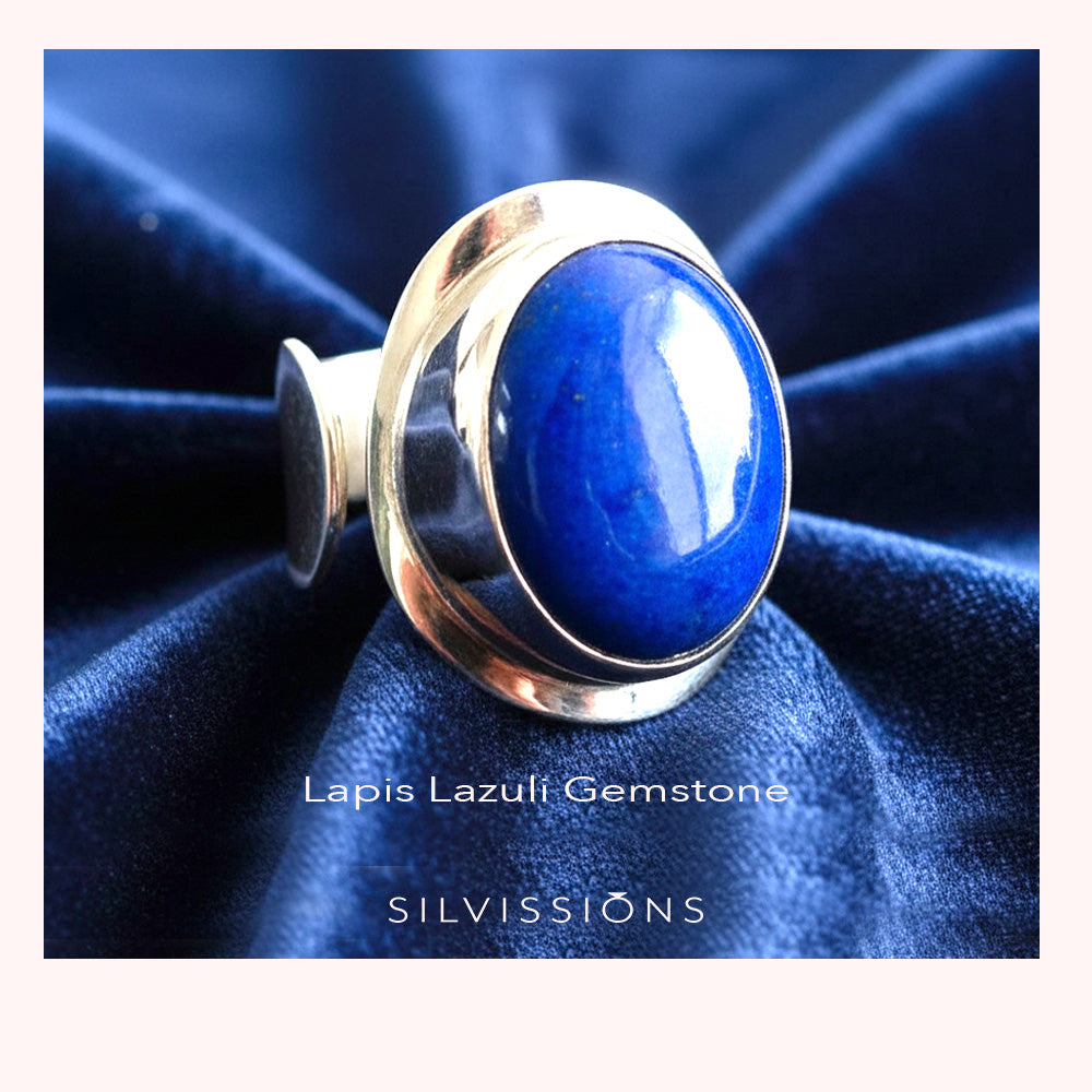 Silver ring with a blue stone on a dark blue fabric background, featuring the brand 'Silvissions'. 