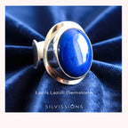 Silver ring with a blue stone on a dark blue fabric background, featuring the brand 'Silvissions'. 