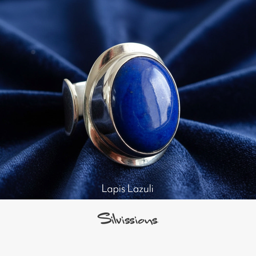 Silver ring with a blue stone on a dark blue fabric background, featuring the brand 'Silvissions'.