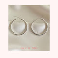 Pair of silver hoop earrings on a blue fabric background with 'Silvissions' branding.