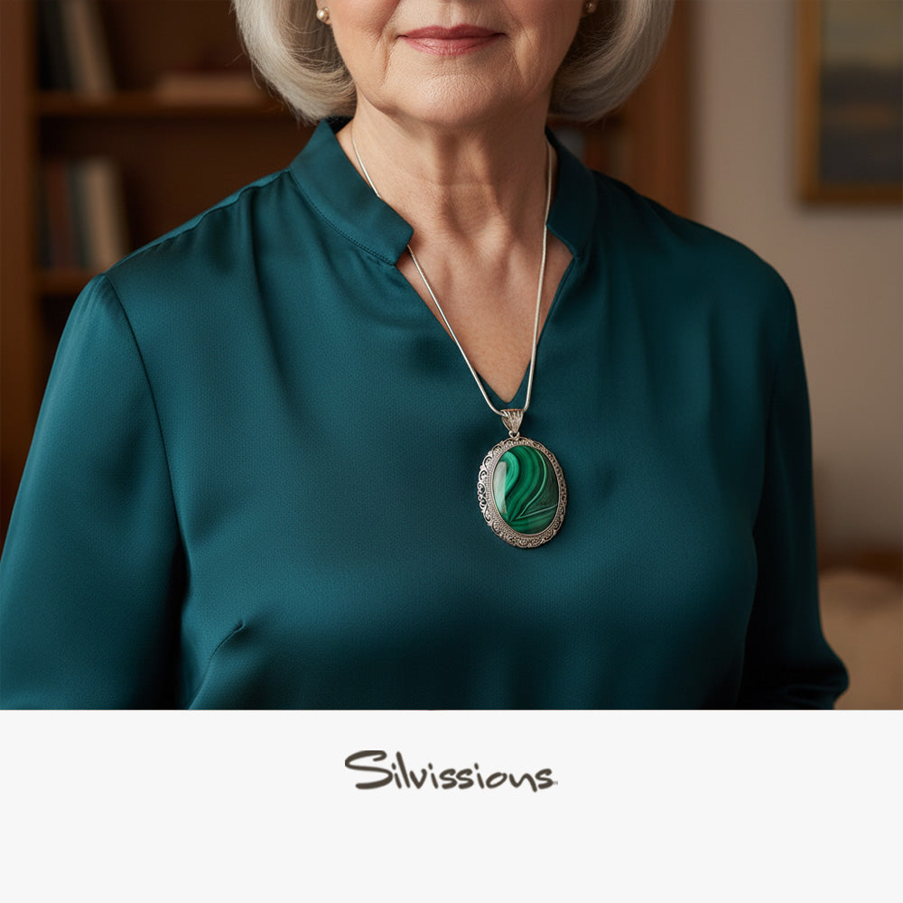 Woman wearing a teal blouse with a necklace featuring a green pendant, blurred background