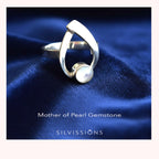 Silver ring with a pearl on a blue fabric background, featuring the brand 'Silvissions'.