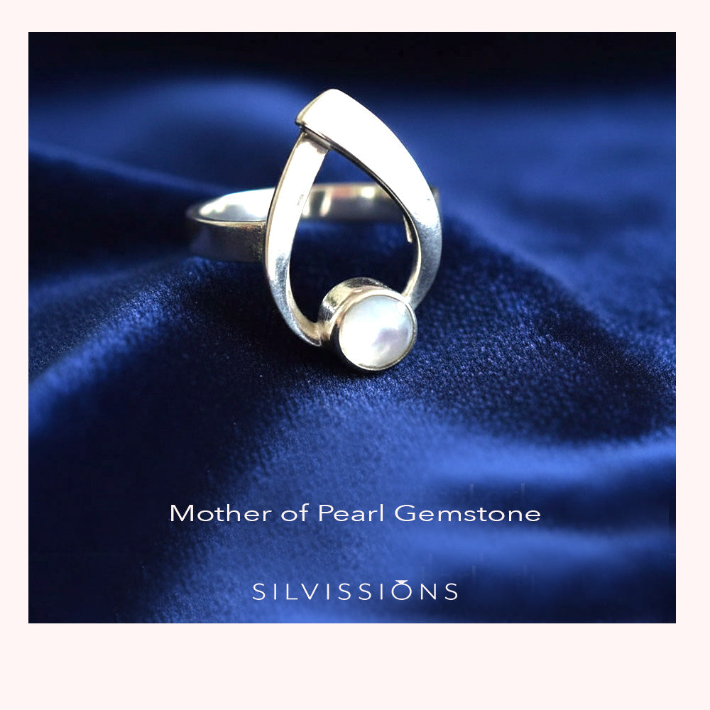 Silver ring with a pearl on a blue fabric background, featuring the brand 'Silvissions'.