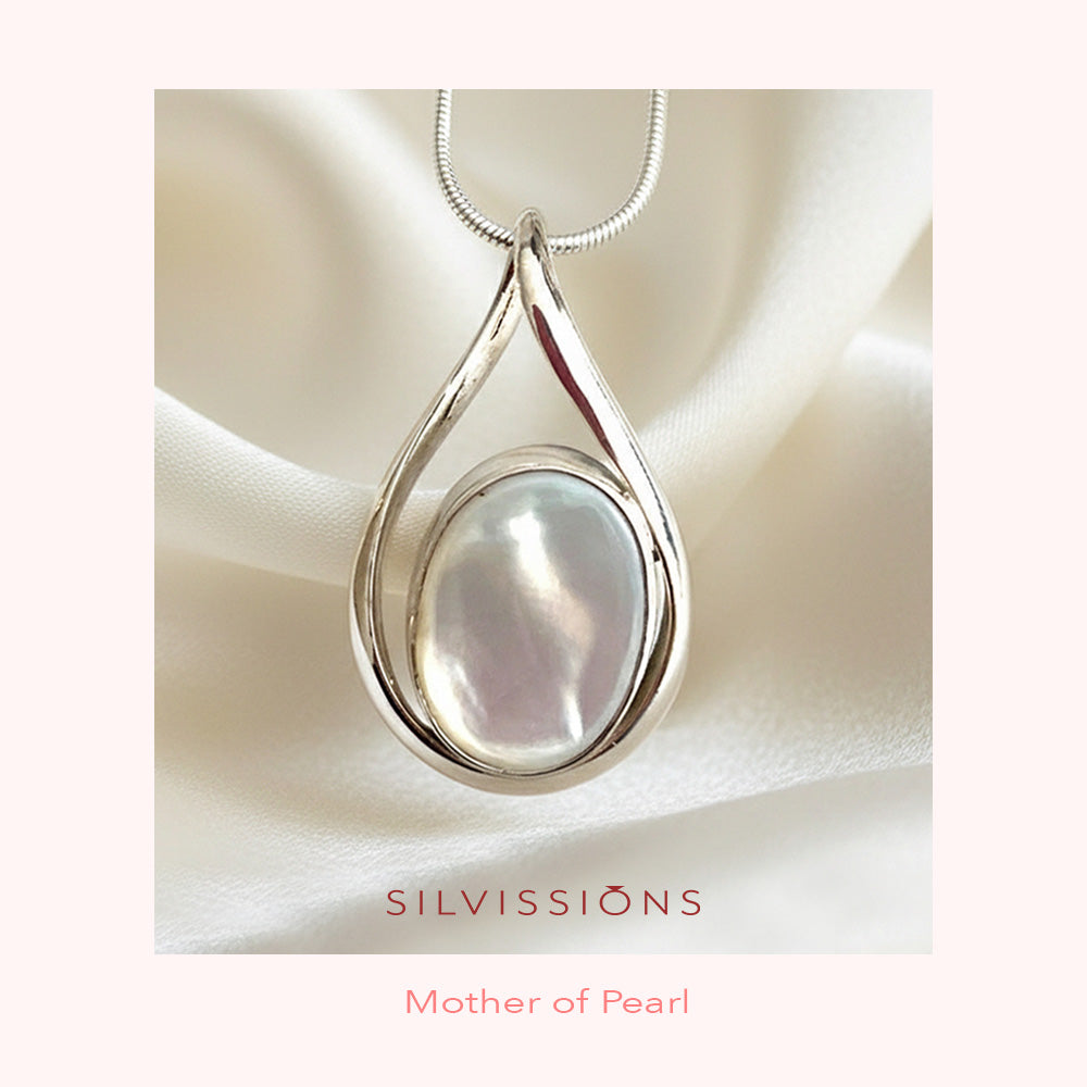Silver pendant with a mother of pearl stone center on a soft fabric background, branded 'Silvissions'.
