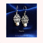 Silver lotus flower earrings with pearls on a blue satin background, branded 'Silvissions'.