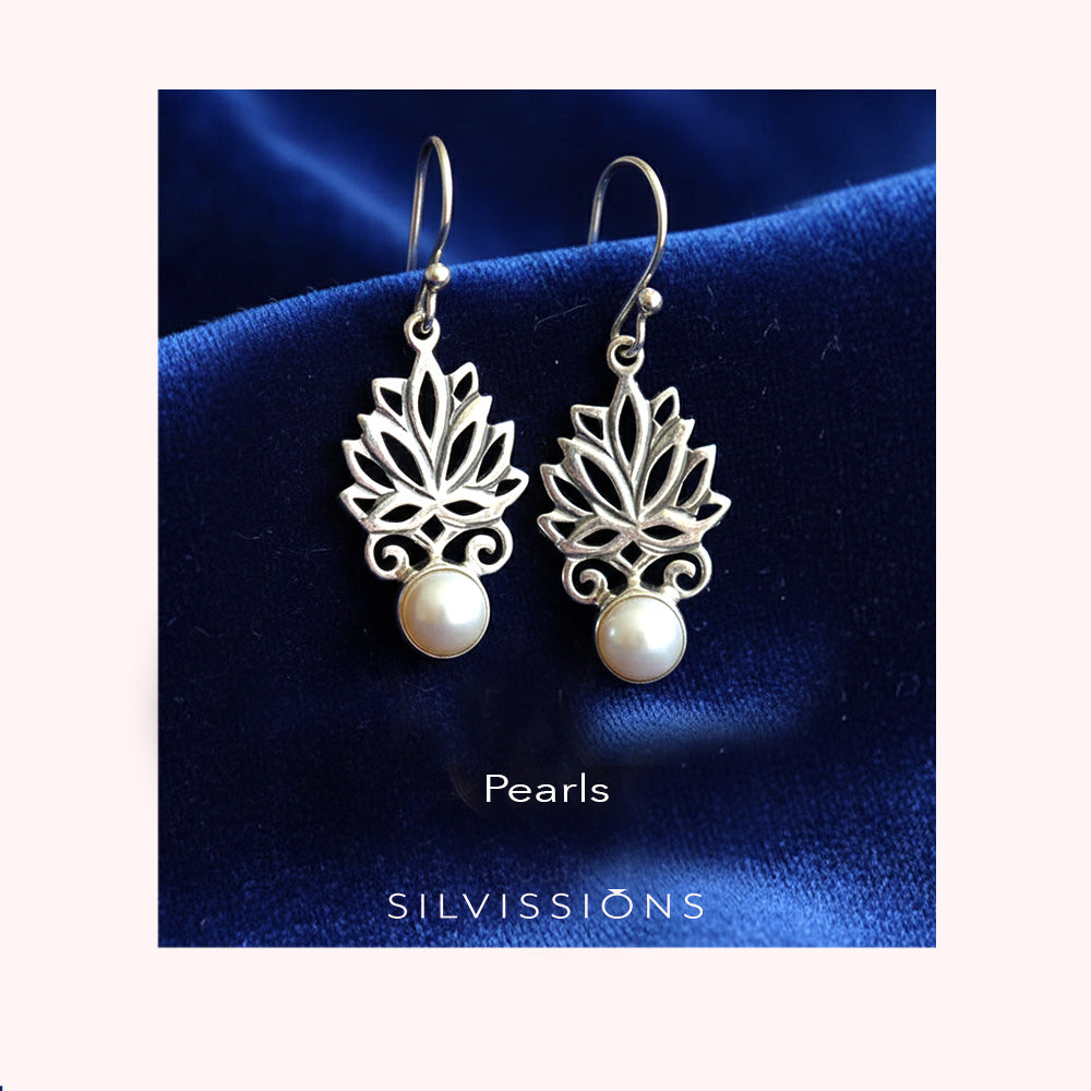 Silver lotus flower earrings with pearls on a blue satin background, branded 'Silvissions'.