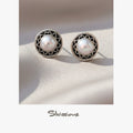 Pair of pearl earrings with silver and black decorative frames on a soft beige background