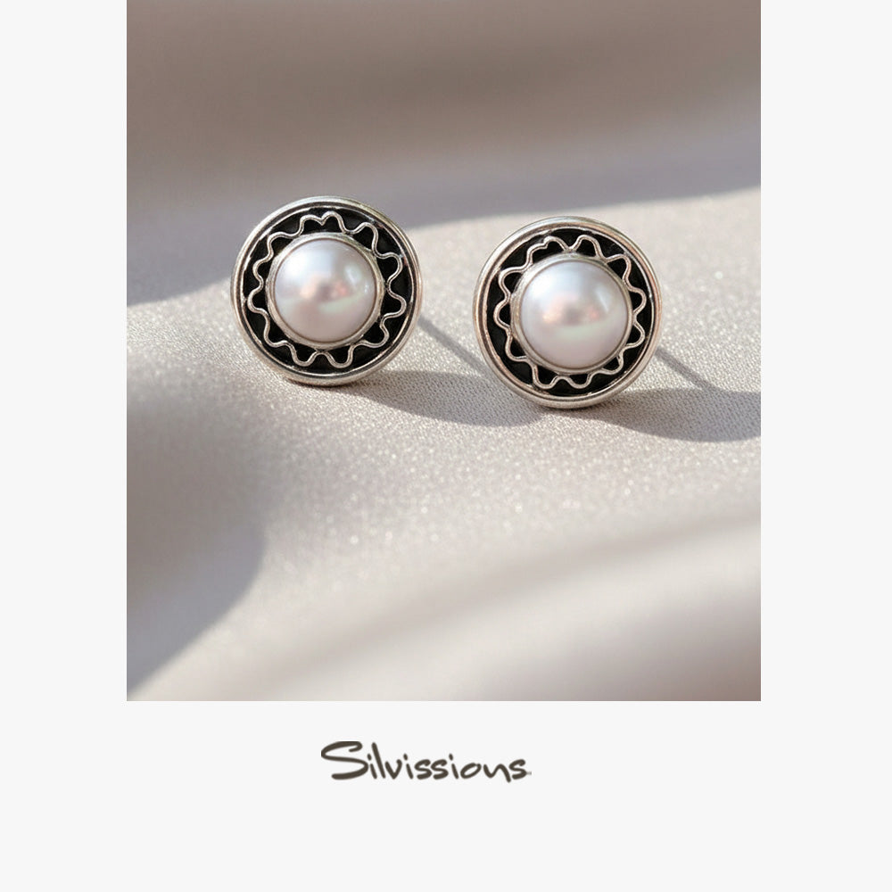 Pair of pearl earrings with silver and black decorative frames on a soft beige background