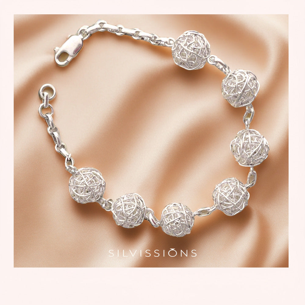 Silver ball bracelet with spherical designs on a beige fabric background, featuring the brand 'Silvissions'.