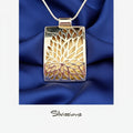 Silver and gold pendant with 'Silvissions' branding on a blurred background