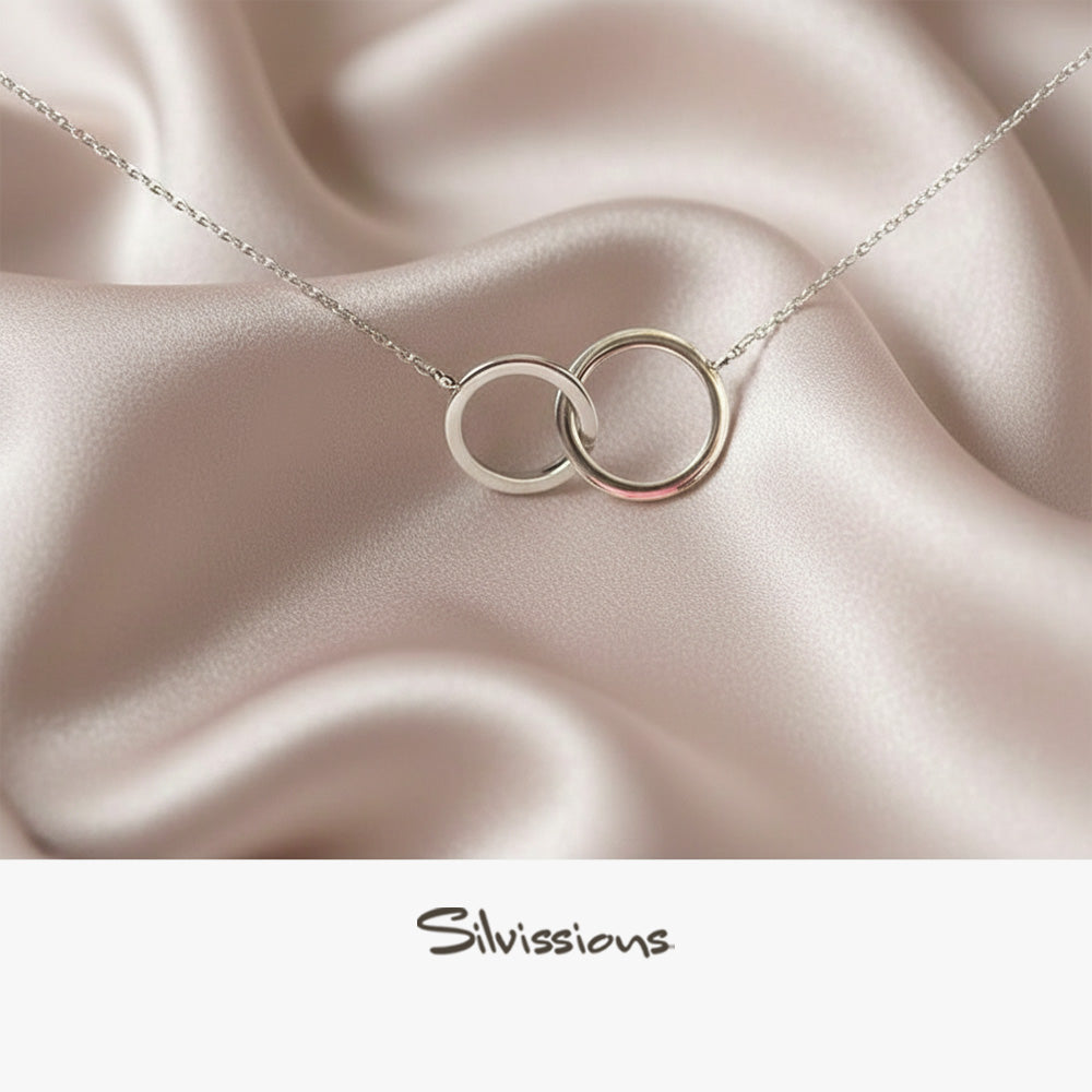 Silver necklace with interlocking rings on a burgundy fabric background, featuring the brand 'Silvissions'.