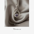 Silver pendant with purple gemstone on a card with flowers in the background, featuring the brand 'Silvissions'.