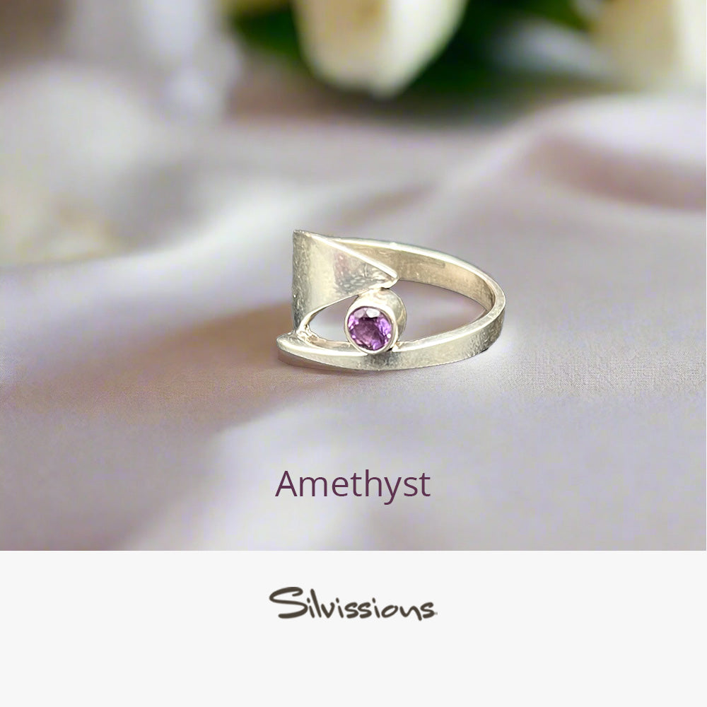 Silver ring with a purple gemstone on a soft fabric background, featuring the brand 'Silvissions'.
