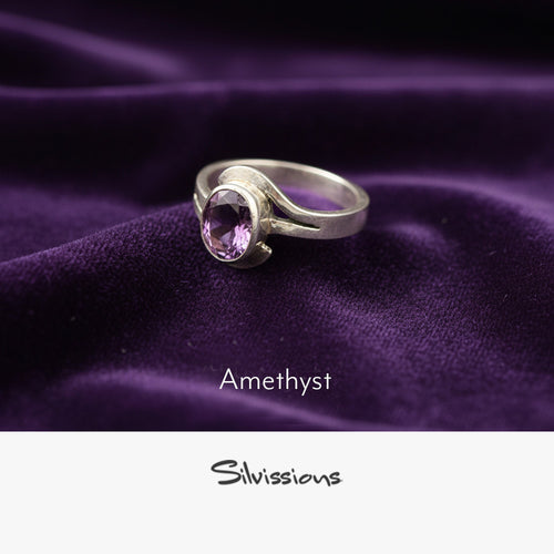 Silver ring with amethyst gemstone on purple fabric, branded 'Silvissions'.