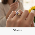 Close-up of a hand wearing a gold and silver ring with a purple gemstone, blurred background with 'Silvassions' branding.