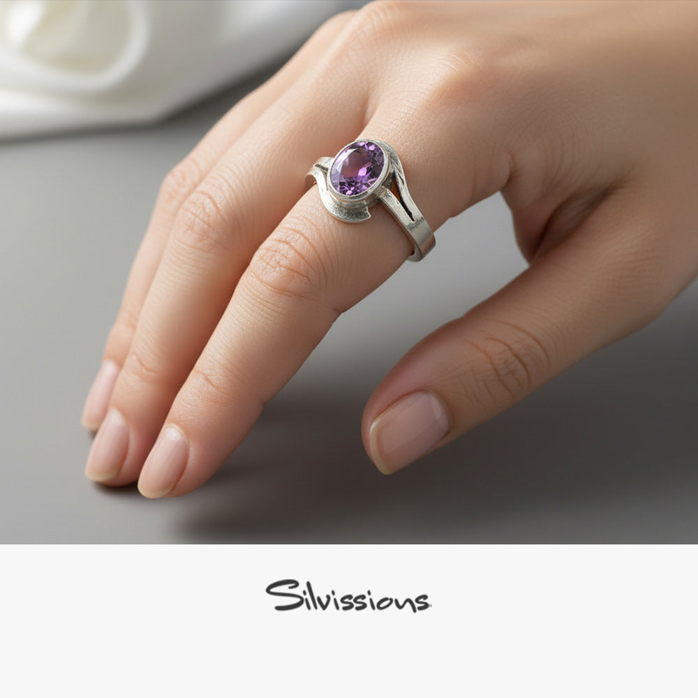 Hand wearing a silver ring with a purple gemstone on a neutral background, featuring the brand 'Silvissions'.