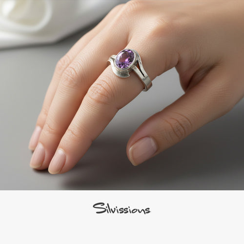 Hand wearing a silver ring with a purple gemstone on a neutral background, featuring the brand 'Silvissions'.